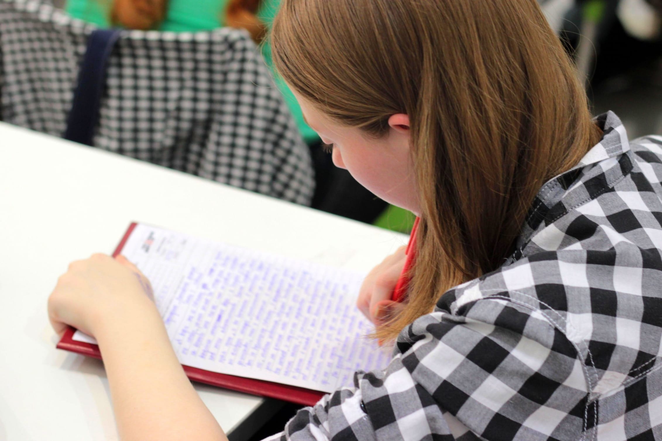Young girl with red hair wearing a black and white checked shirt, writing in a notebook
