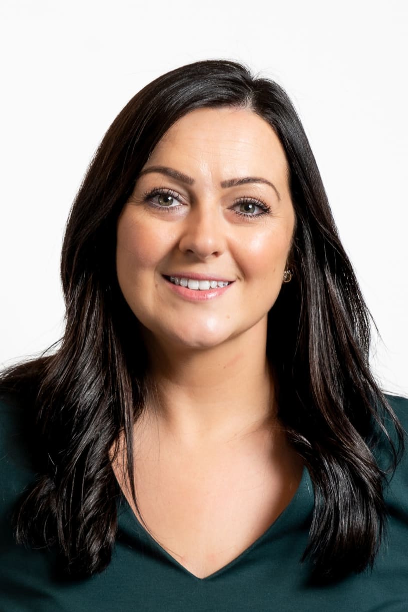 Lisa Gilbert, Interim Head of Communications; woman smiling at camera with long dark brown hair wearing a dark green top